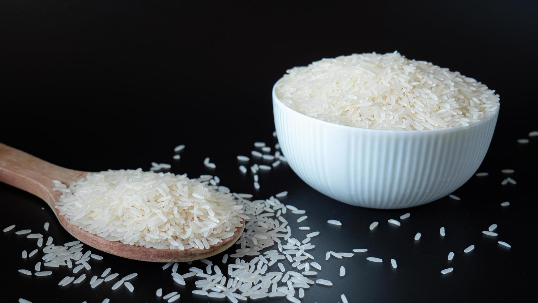 Jasmine rice, popular rice variety in Thailand. Rice grain that has passed through the polishing process Ready to be cooked or steamed. White seeds on black background. photo