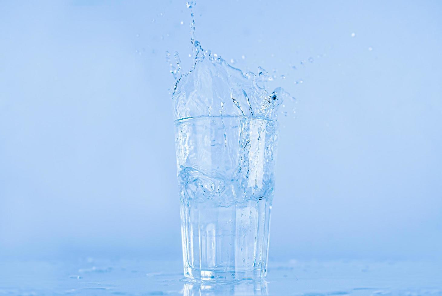 A glass of water splashed up. The water rose from a clear glass with a square. photo