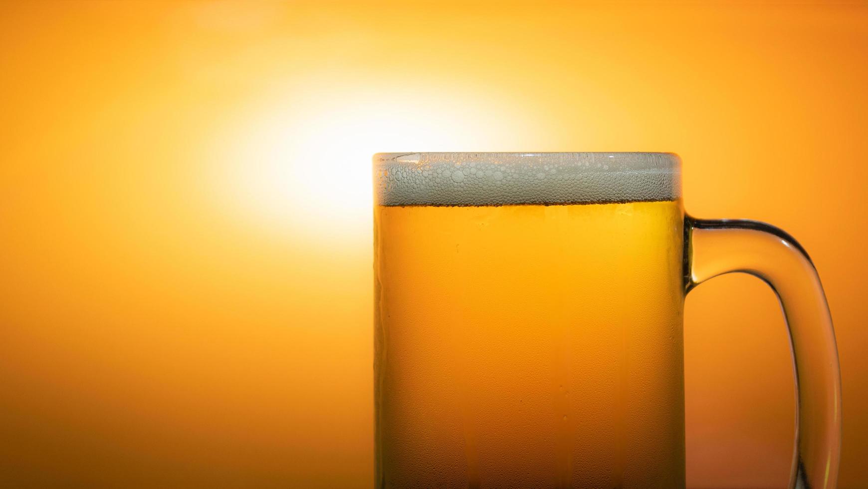 Pour the beer into a clear glass with beer foam and bubble. Golden orange light background. photo