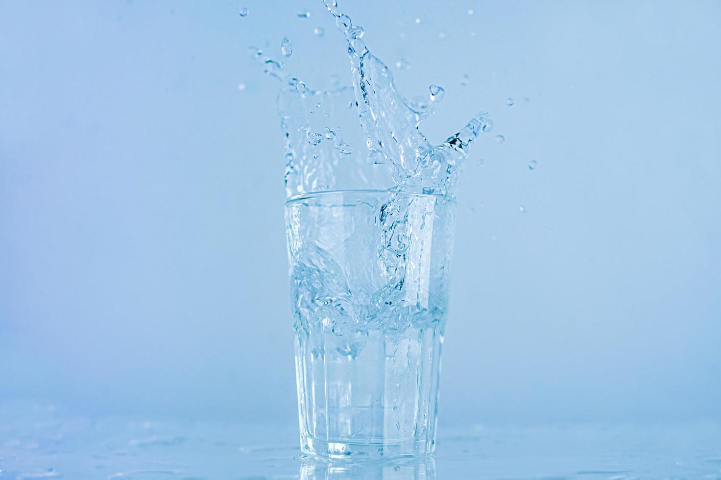 A glass of water splashed up. The water rose from a clear glass with a square. photo