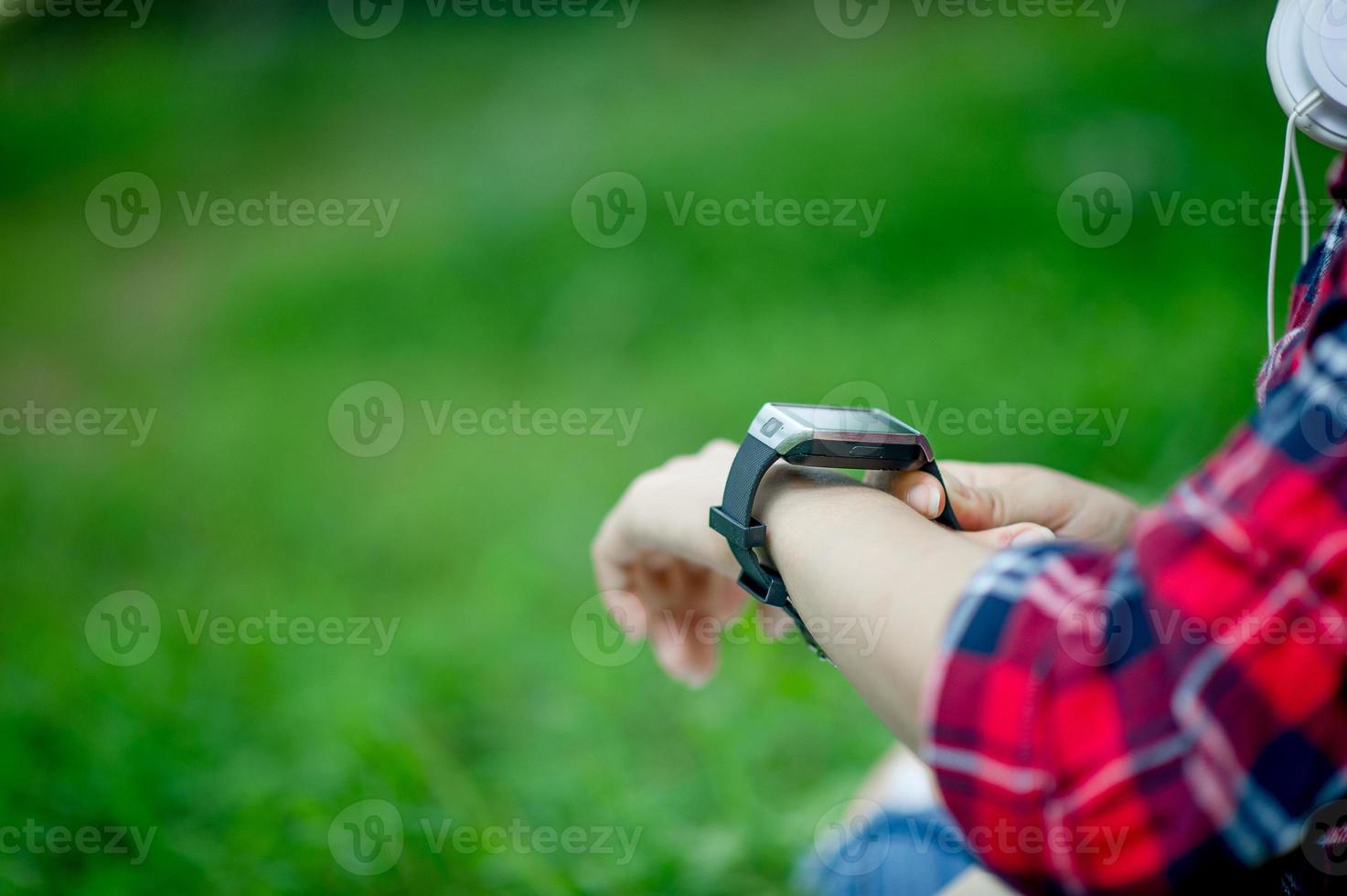 la niña mira el reloj en la mano, mira la hora en un reloj negro, usa una camisa roja y un fondo verde. y hay un espacio de copia. foto