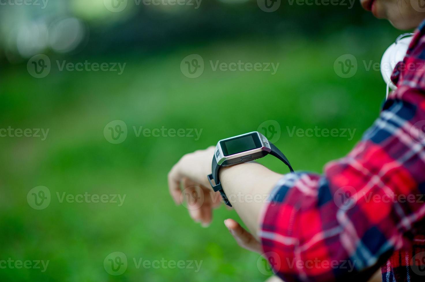 The girl watches the watch in hand, watches the time in a black watch, wears a red shirt and a green background. And there is a copy space. photo