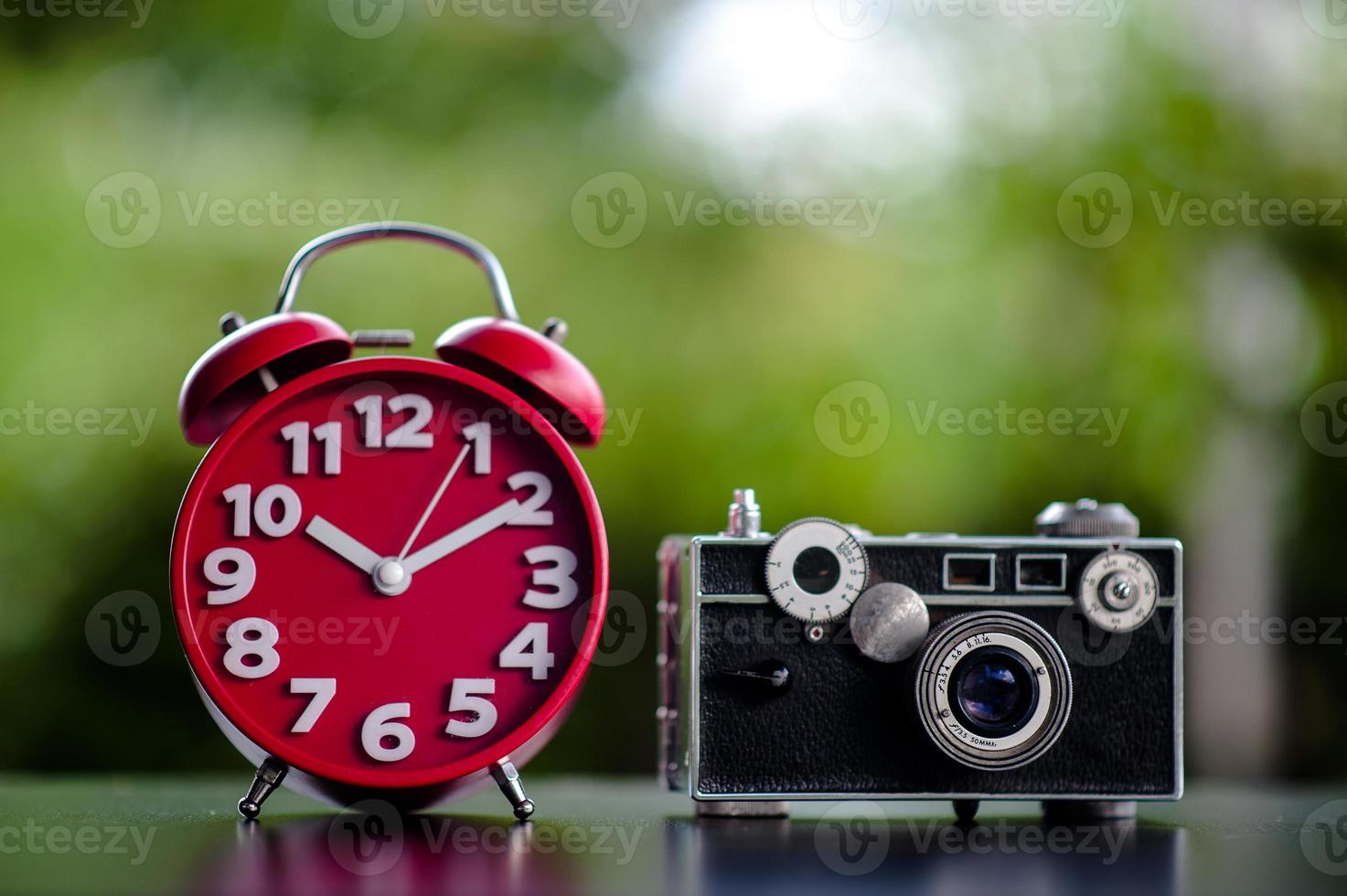el reloj rojo y la cámara ponen sobre la mesa el tiempo y los conceptos de equipo de tiro de puntualidad y fotografía foto