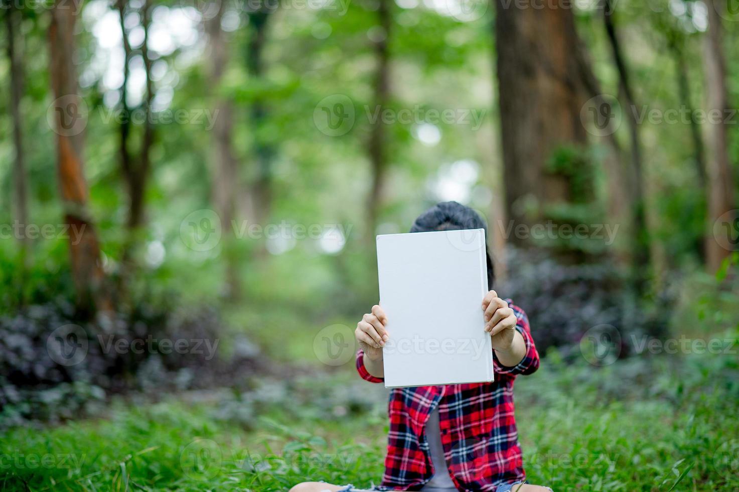 Girl holding a4 paper in under the green tree. And there is a copy space. photo