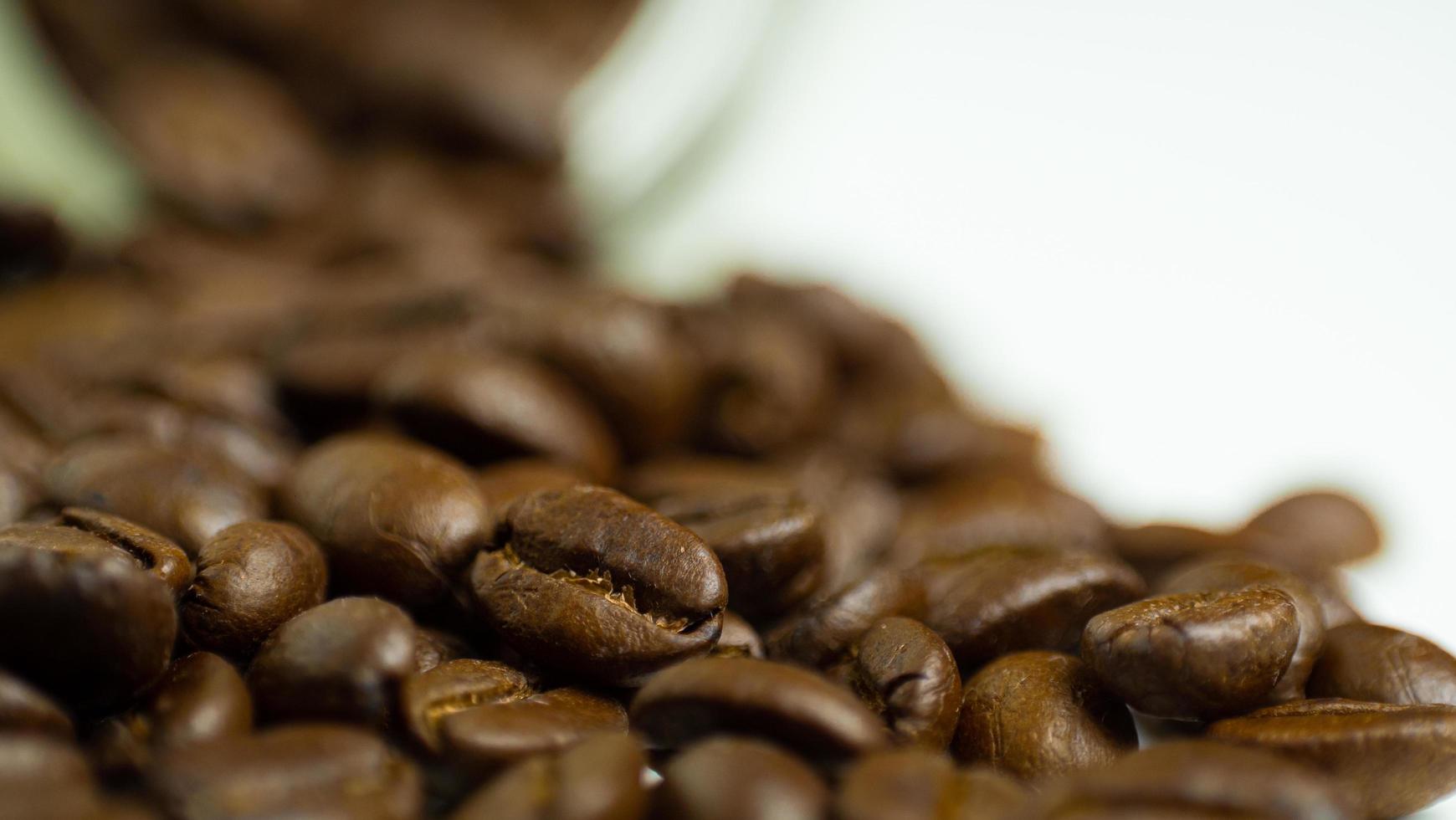 los granos de café tostados se preparan para la molienda que se vierte de una botella de vidrio colocada sobre un fondo blanco para hacer café recién hecho o entrar en una máquina de espresso o en una cafetera moka foto