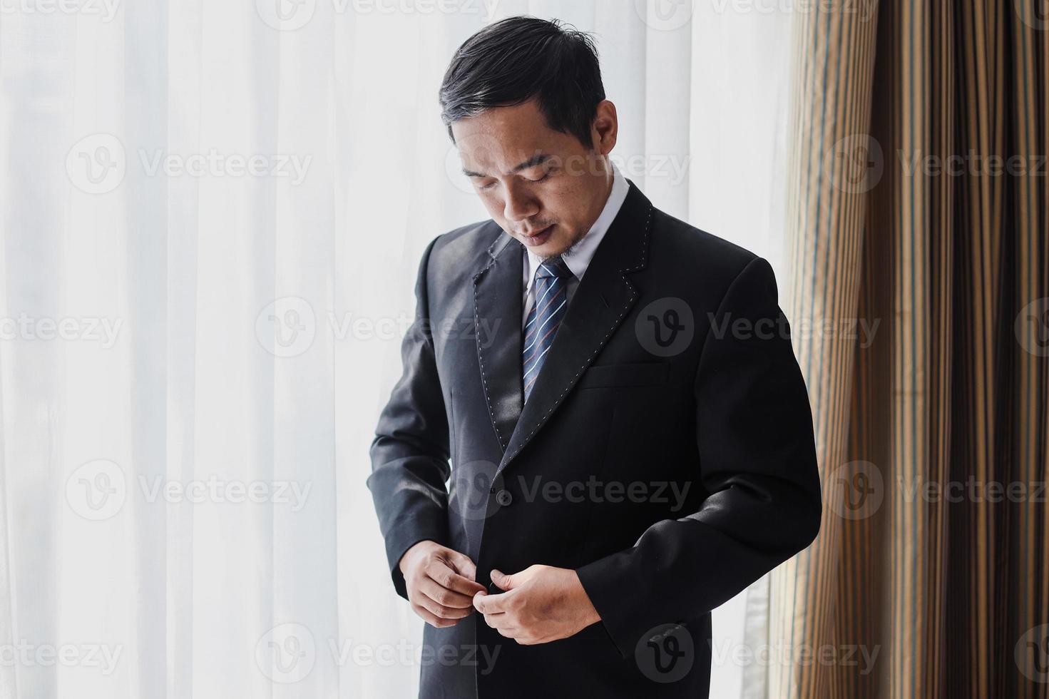 Asian man or groom buttoning his black suit photo