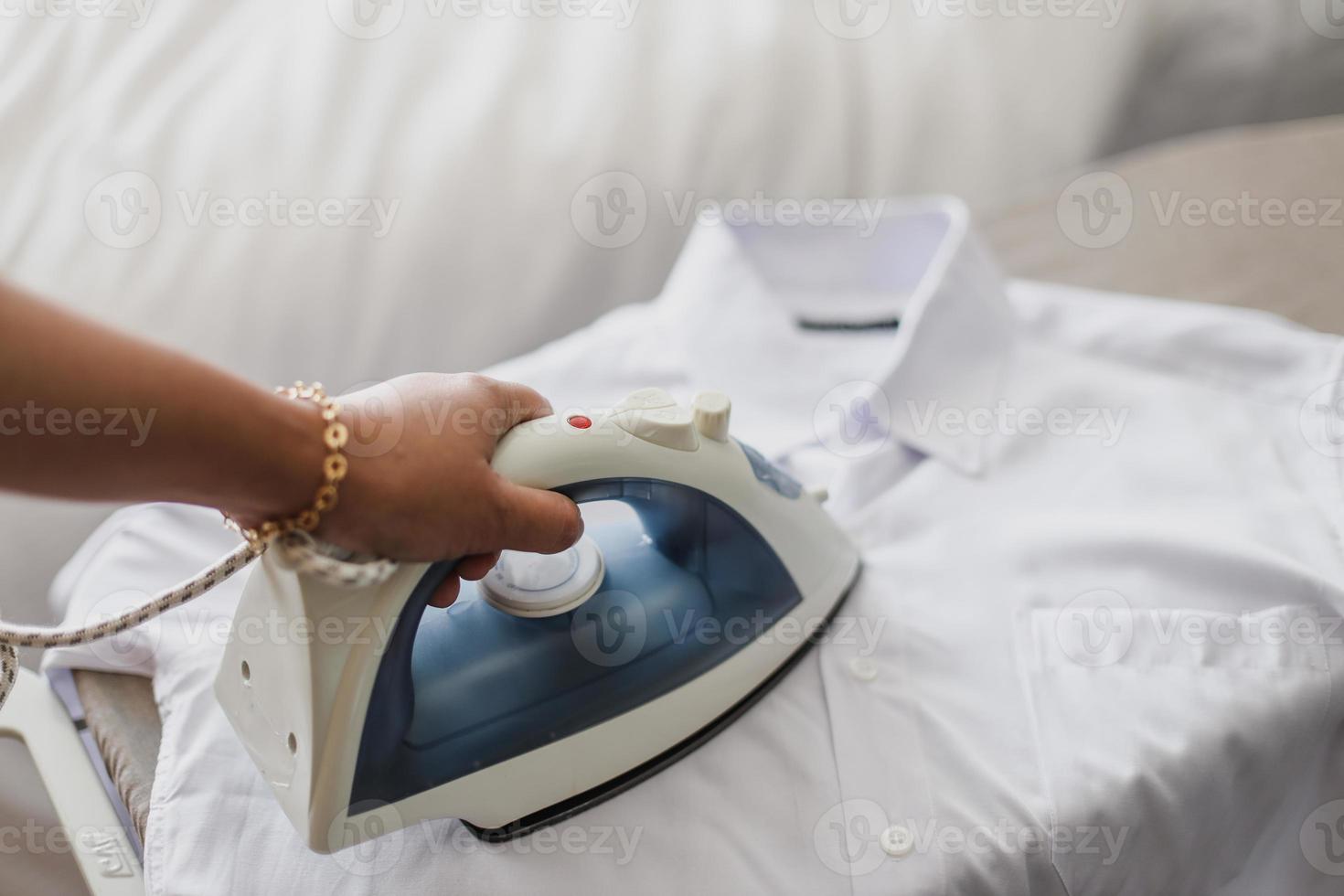 Female hand ironing white shirt on ironing board photo