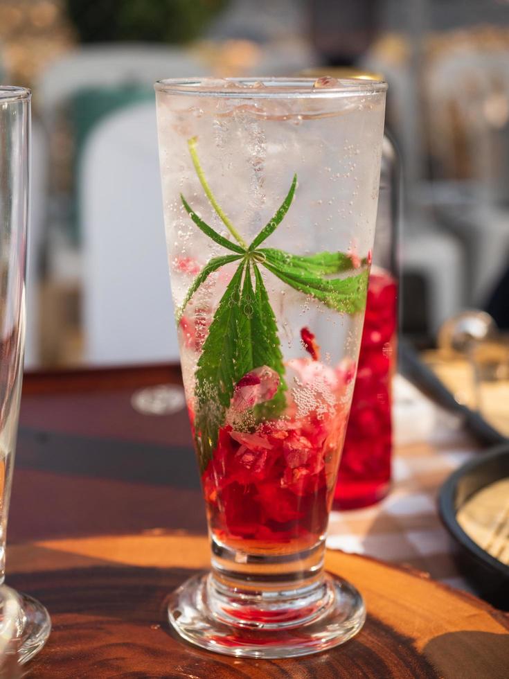 A glass of cold red Italian soda with marijuana or cannabis leaf. photo