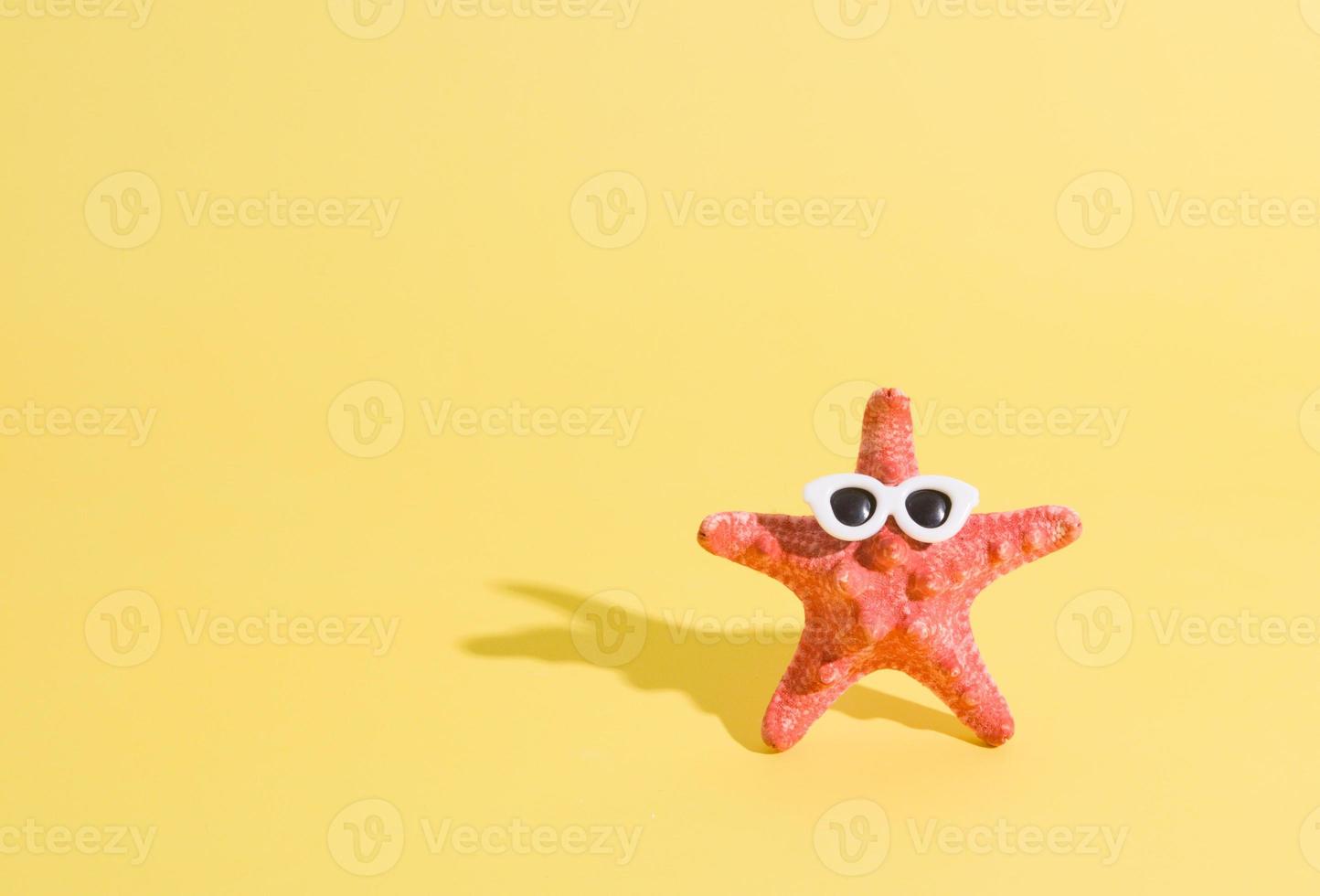 Starfish in sunglasses on a yellow background. Minimalistic humorous summer concept with copy space photo