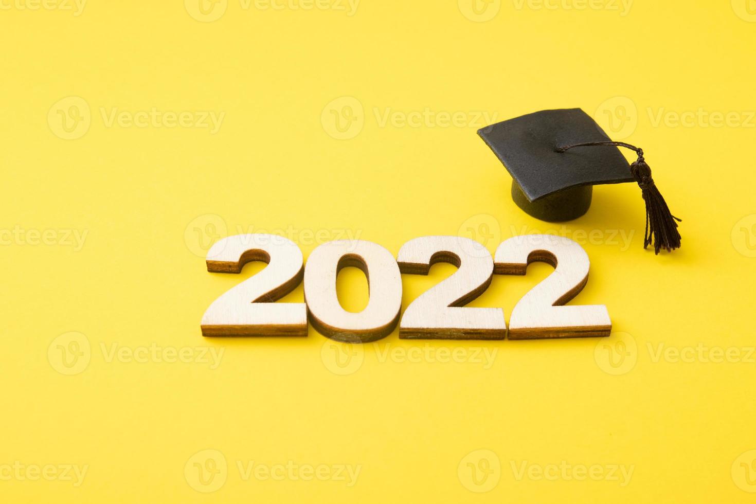 Graduat hat with wooden number 2022 on yellow background. Leaning, class 2022 concept photo