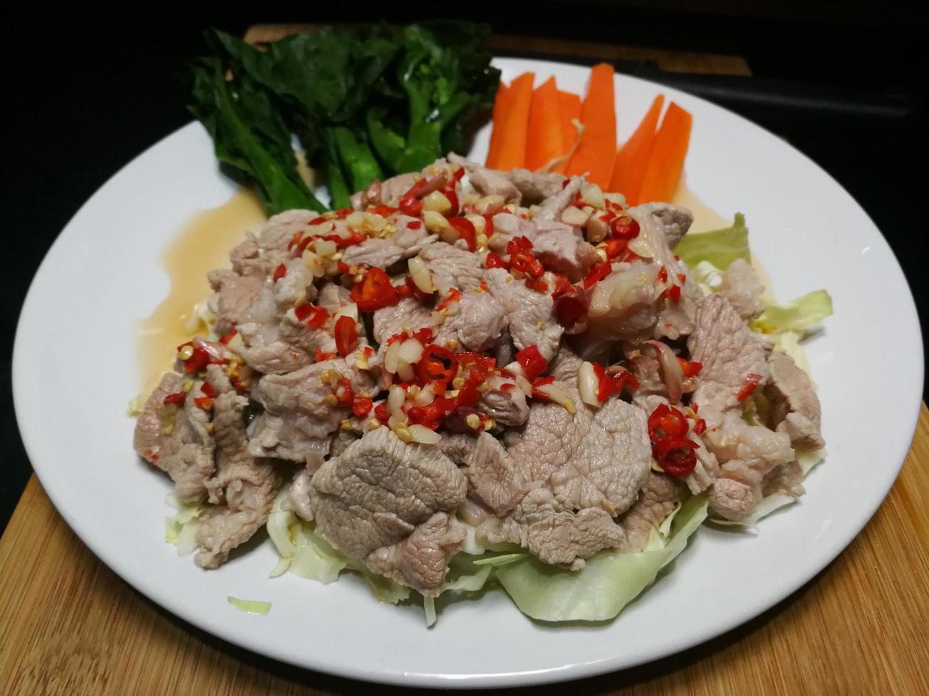 Pork with Lemon spicy-sweet sauce with chili and garlic mixed with sour lemon juice. Arrange the dish with kale and carrots on a white plate placed on a wooden chopping board. photo