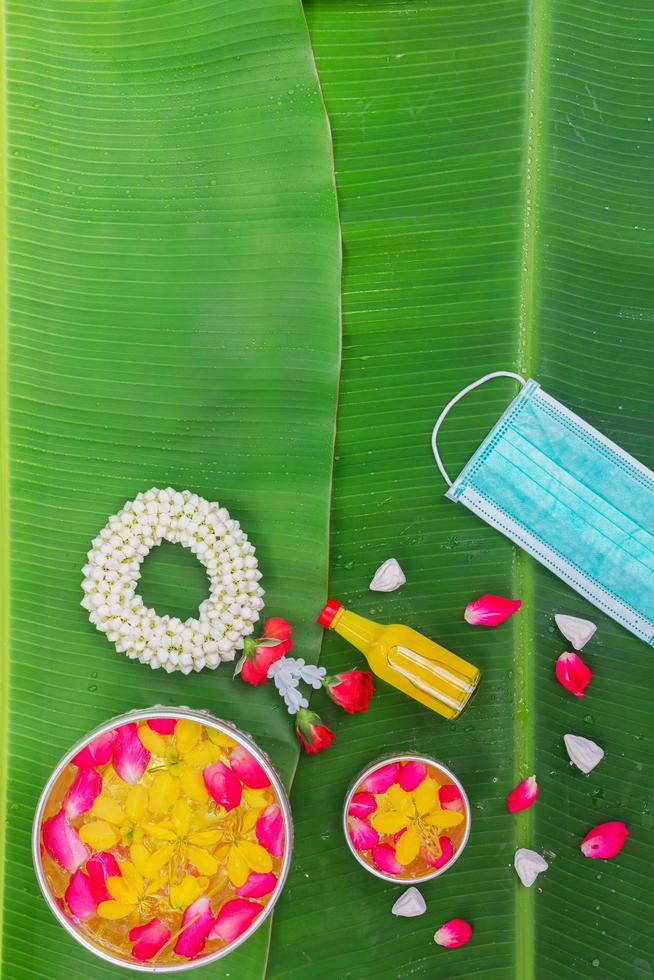 Songkran Festival background with jasmine garland Flowers in a bowl of water, perfume and limestone on a green wet banana leaf background. photo