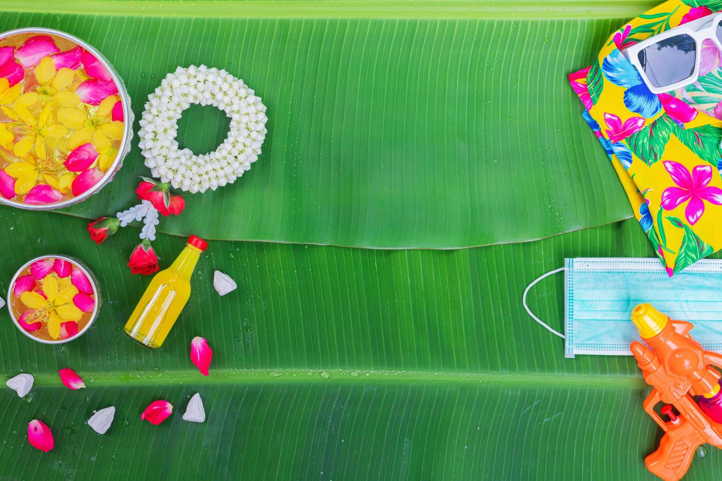 fondo del festival songkran con flores de guirnalda de jazmín en un tazón de agua, perfume y piedra caliza sobre un fondo verde de hoja de plátano húmedo. foto