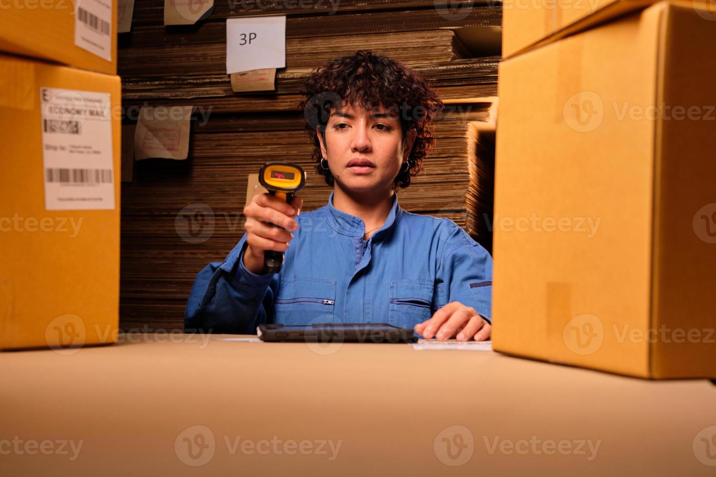 One female worker in safety uniform uses a bar code scanner and tablet to check shipping orders at parcels warehouse, paper manufacture factory for the packing industry, logistic transport service. photo