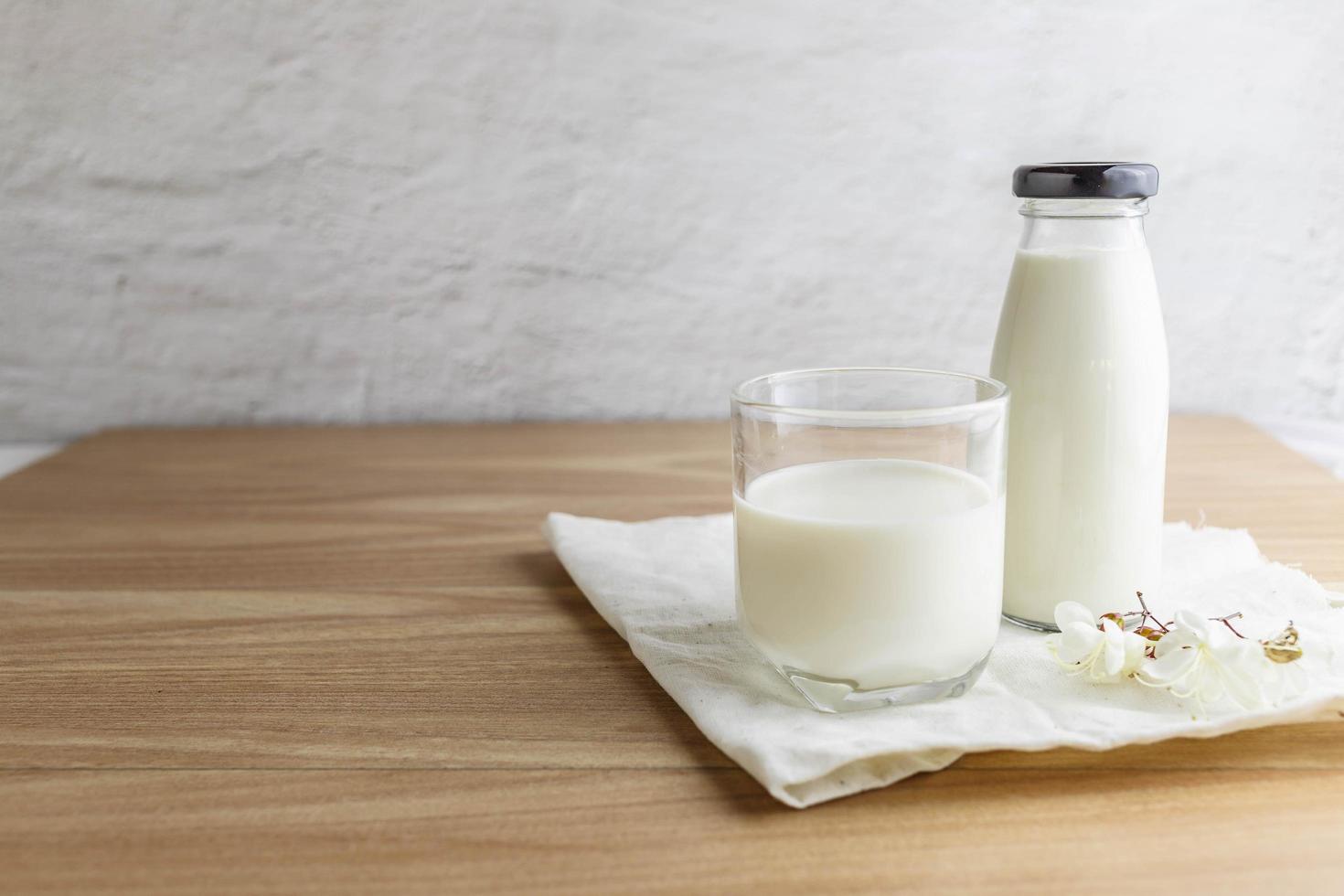 Milk bottle and glass of milk on wooden table photo