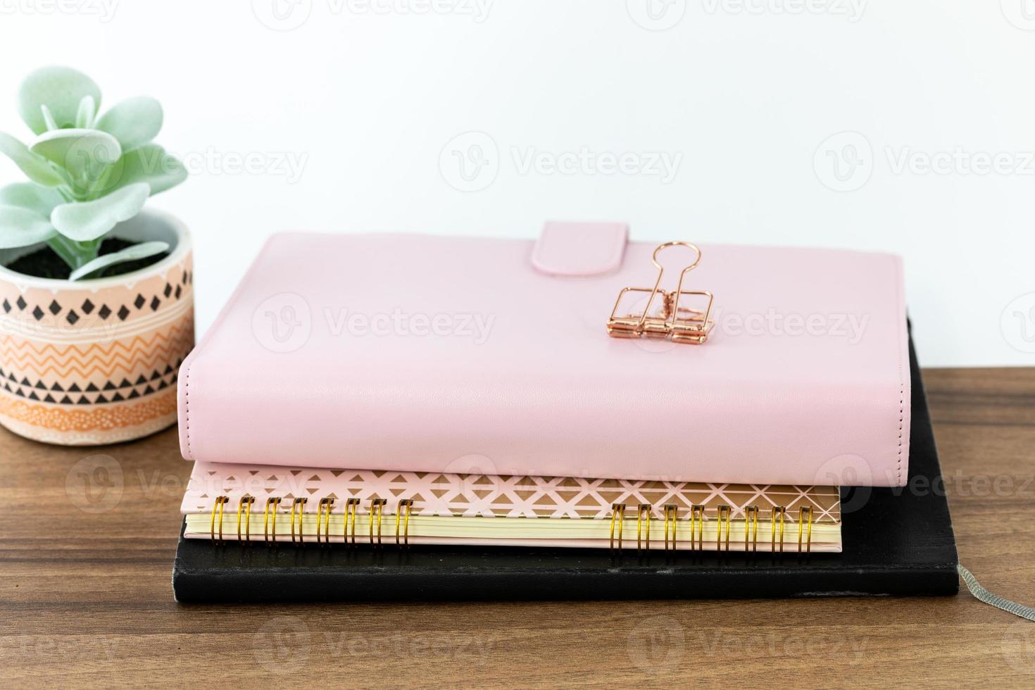 Espacio de trabajo femenino y femenino con organizador rosa, cuaderno de anillos y cuaderno de bocetos de tapa negra sobre una mesa de madera. foto