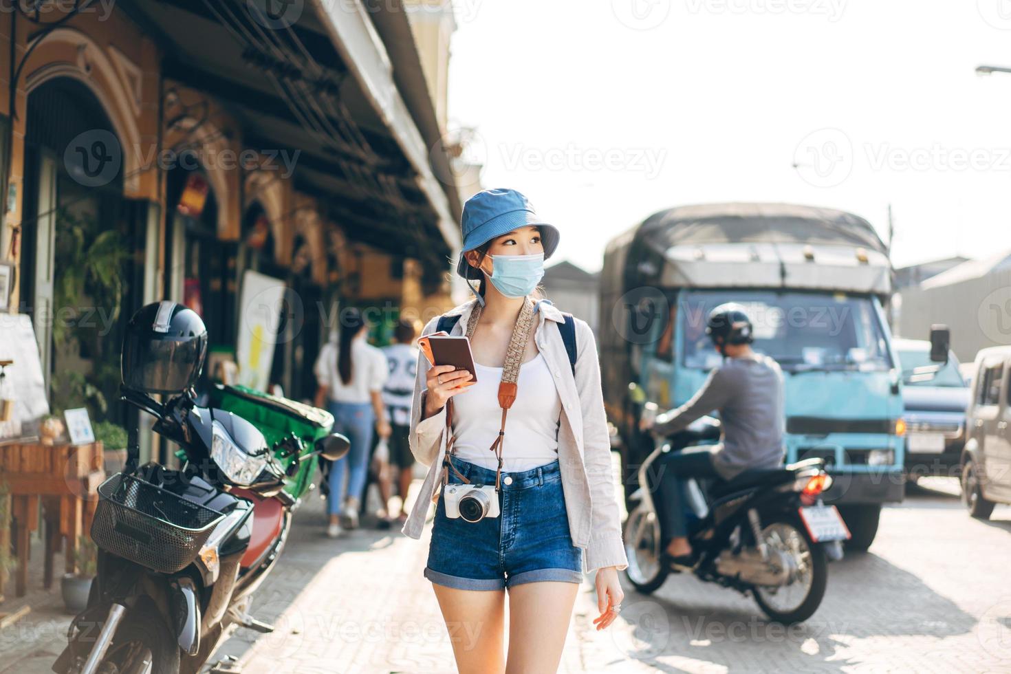 Walking young adult asian woman traveller wear face mask for covid-19 traveling in local city on summer day. photo