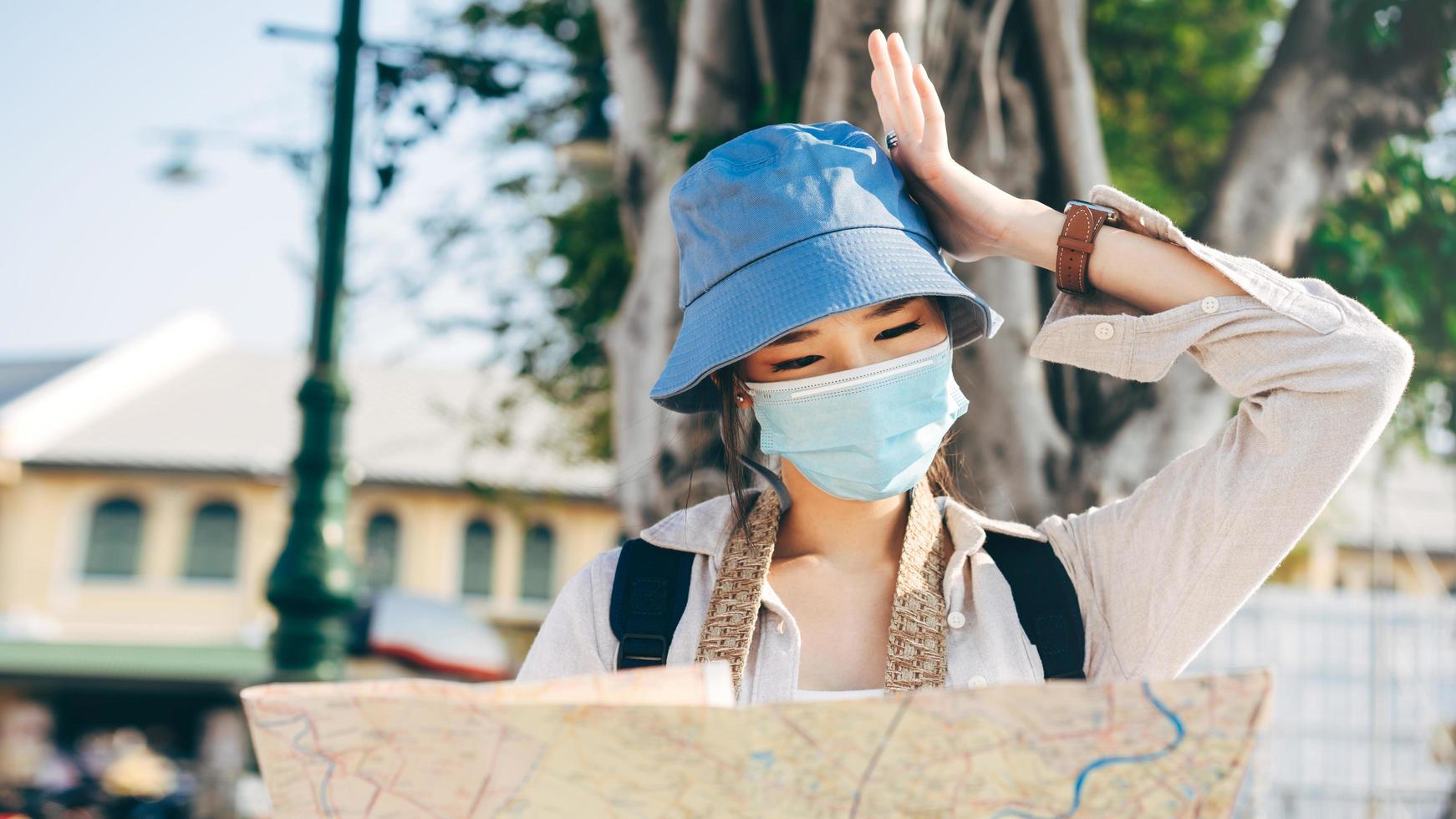 adult traveller asian woman wear face mask for protect virus corona or covid 19 using map for searching destination. photo