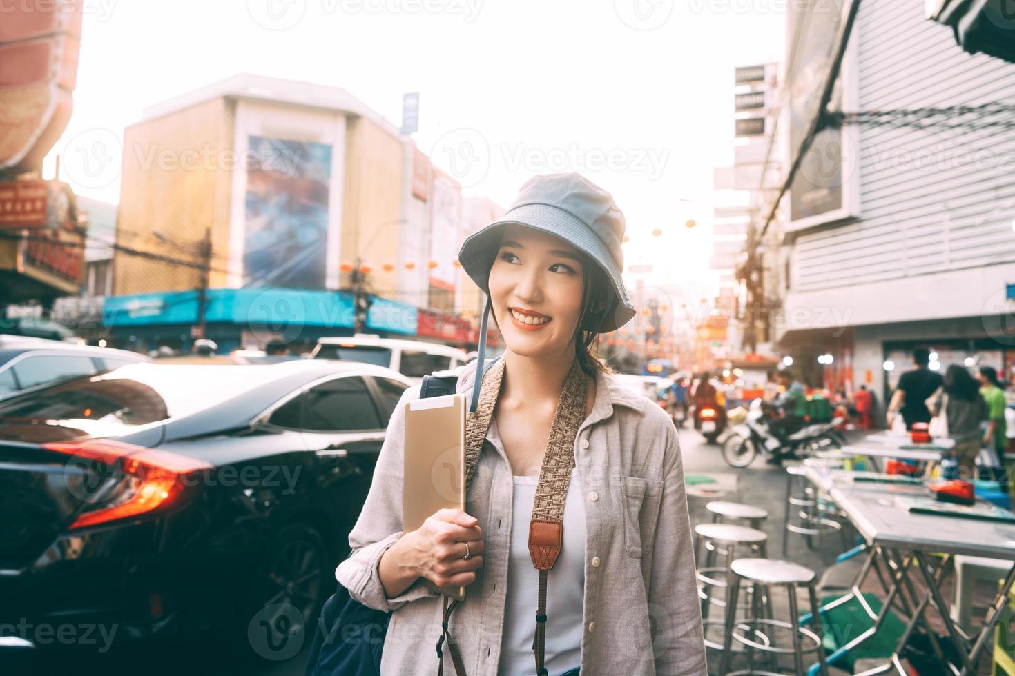 Caminando a una joven adulta asiática que viaja sola viajando con una tableta digital en la ciudad el día. foto