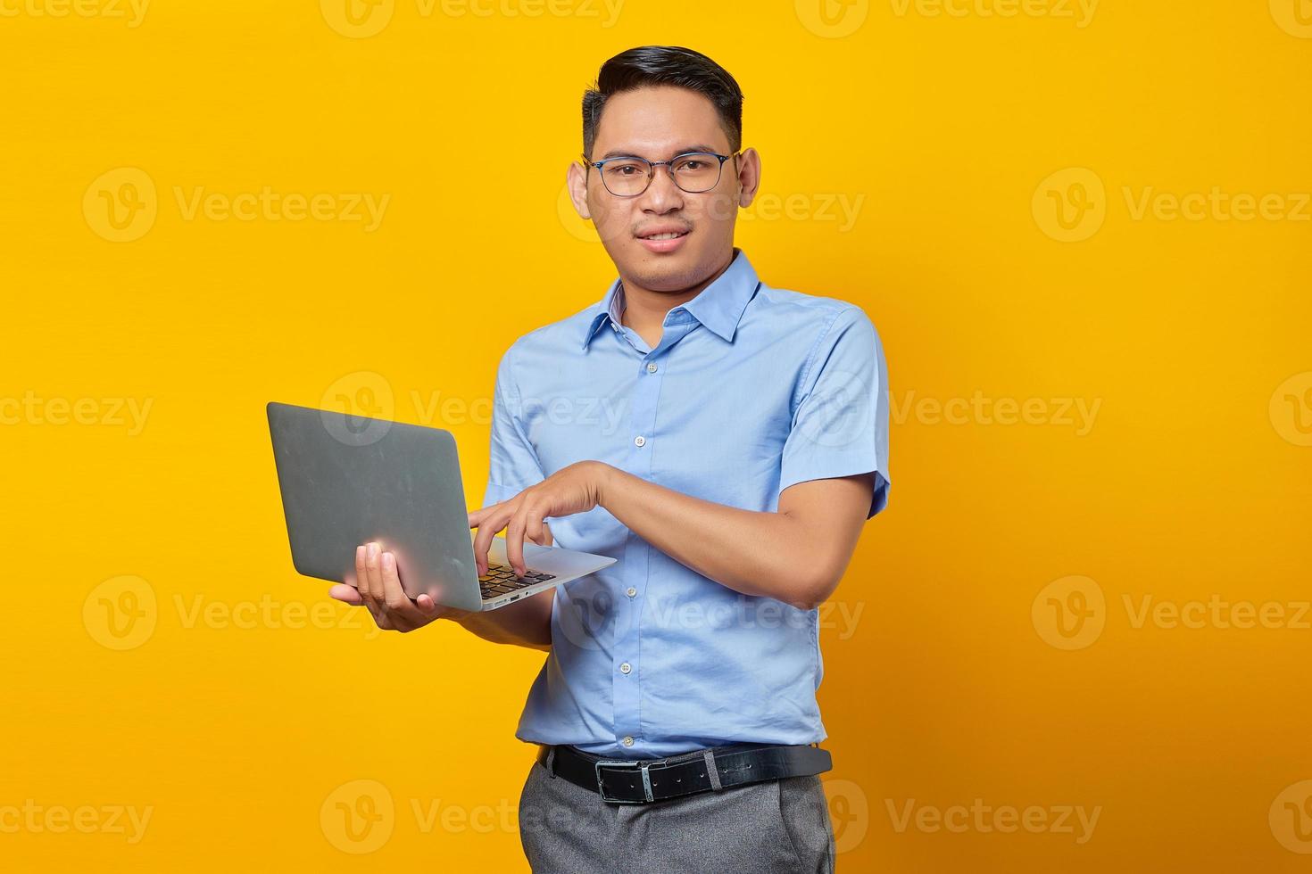 Smiling young asian man Asian in glasses using laptop isolated on yellow background. businessman and entrepreneur concept photo
