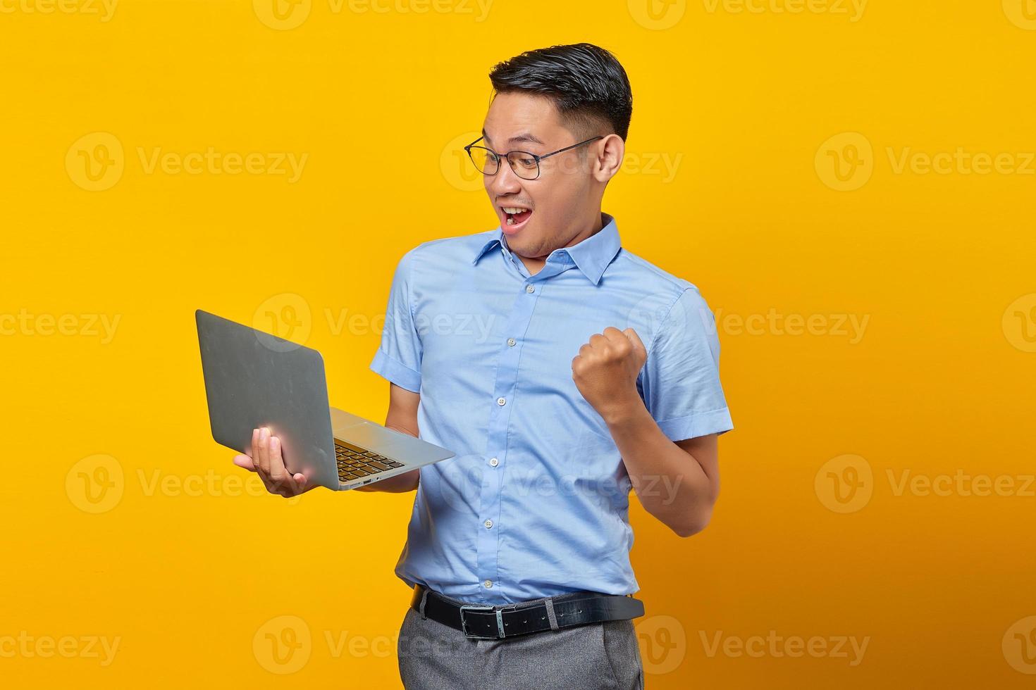 Excited young asian man Asian in glasses using laptop isolated on yellow background. businessman and entrepreneur concept photo