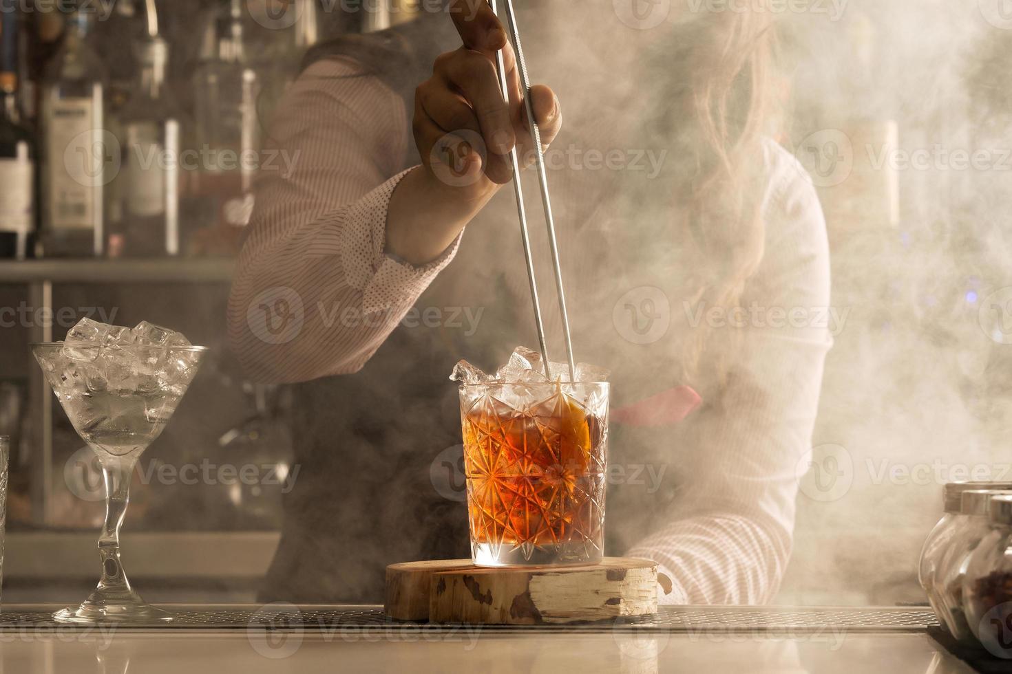 barman con pinzas agregando ingrediente al cóctel foto