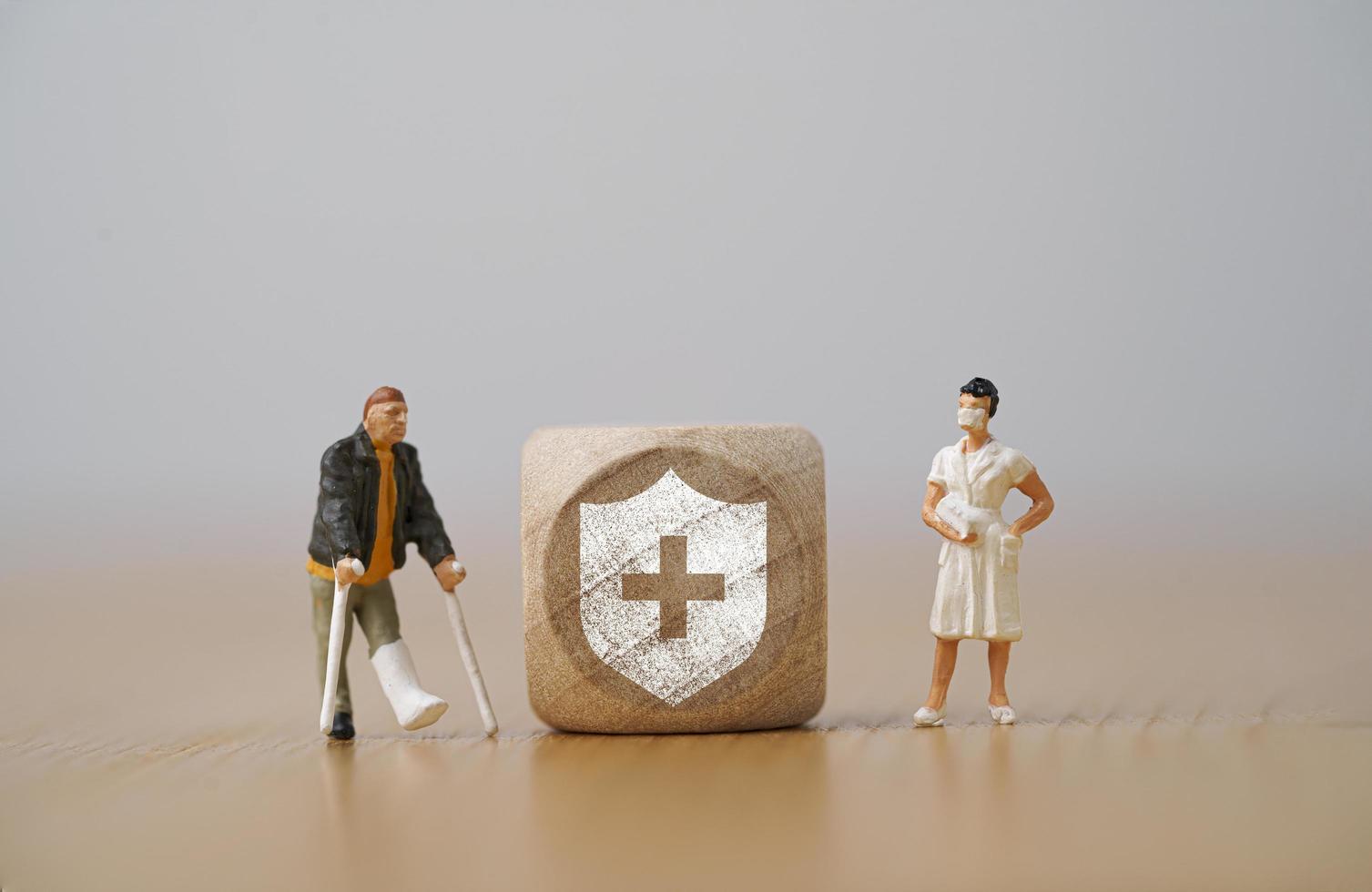 Miniature figure  man with a broken leg uses a crutch standing beside with nurse and insurance sign for healthcare assurance claim and medical concept. photo