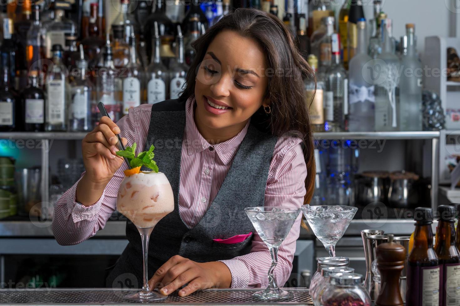 Happy Hispanic woman decorating cocktail in bar photo