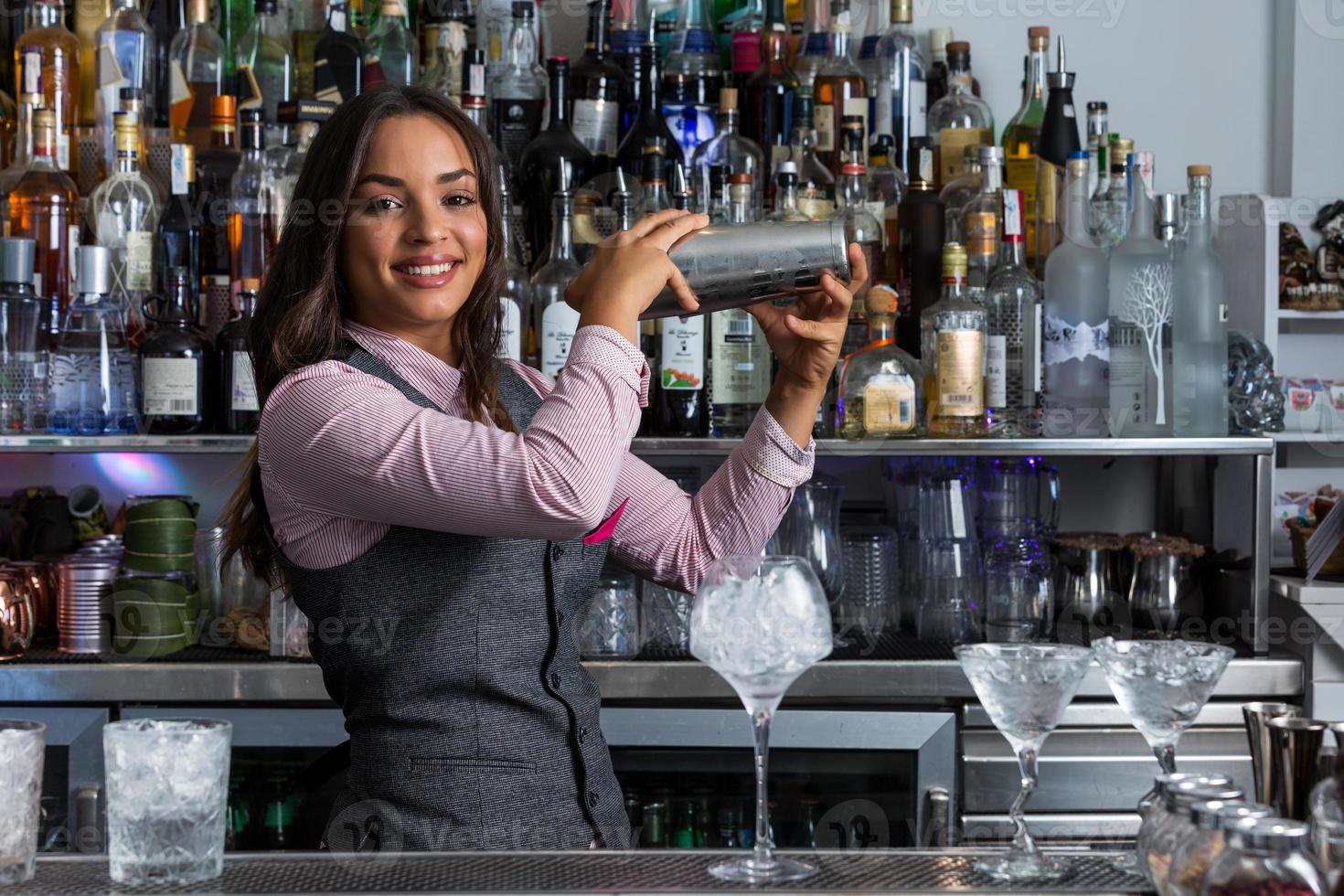 Cheerful female bartender with shaker preparing cocktail photo