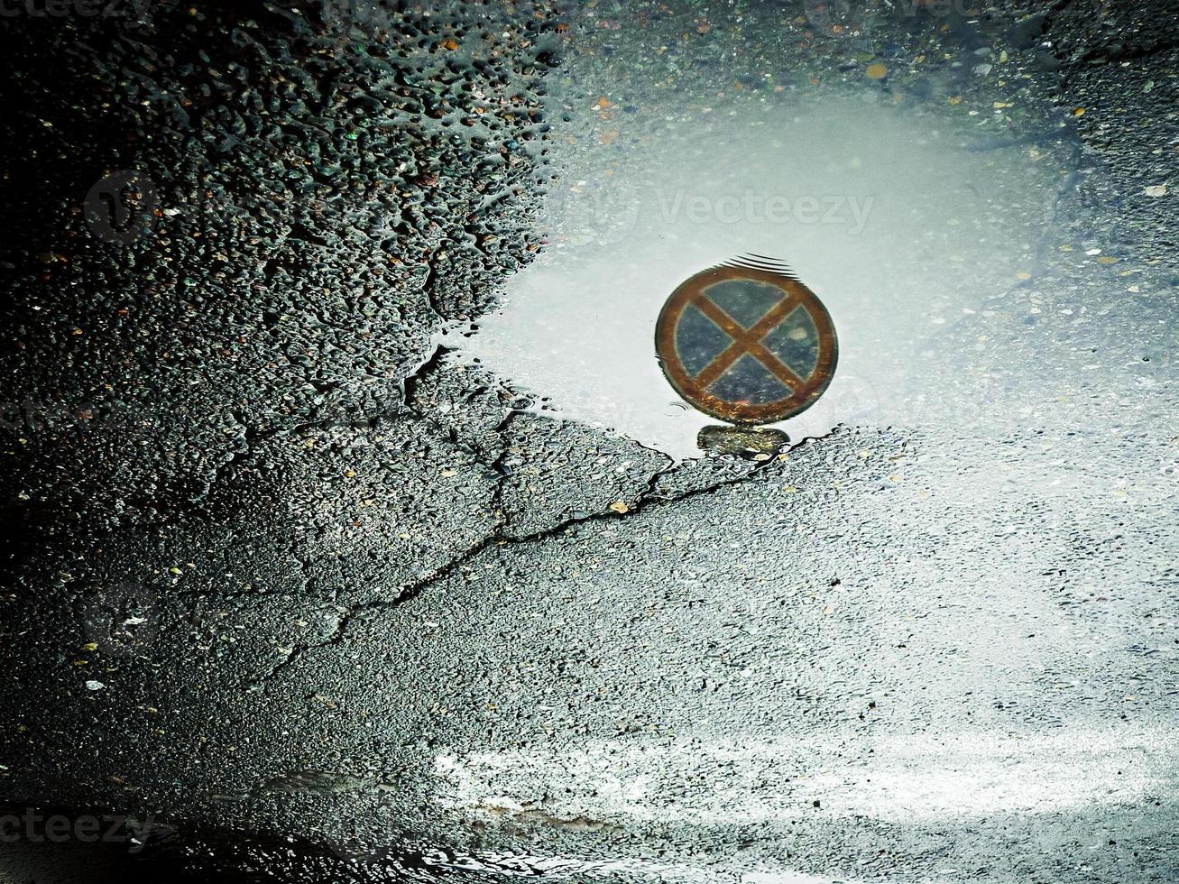 Road sign reflected on water surface. Wet cracked asphalt background with reflection. photo