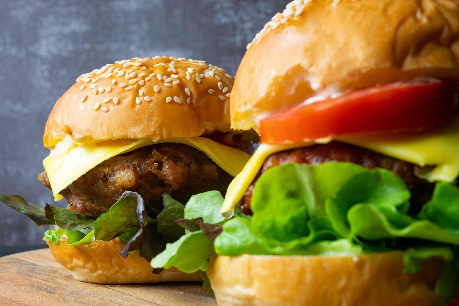 close up two fresh tasty homemade hamburgers with fresh vegetables, lettuce, tomato, cheese beside sliced tomatoes on a cutting board. Free space for text photo