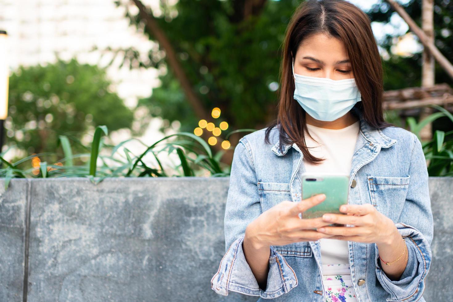 Portrait of a young woman in a medical mask for anti-coronavirus COVID-19 pandemic infectious disease outbreak protection and use a smartphone in Public area. Concept of Virus pandemic and pollution photo