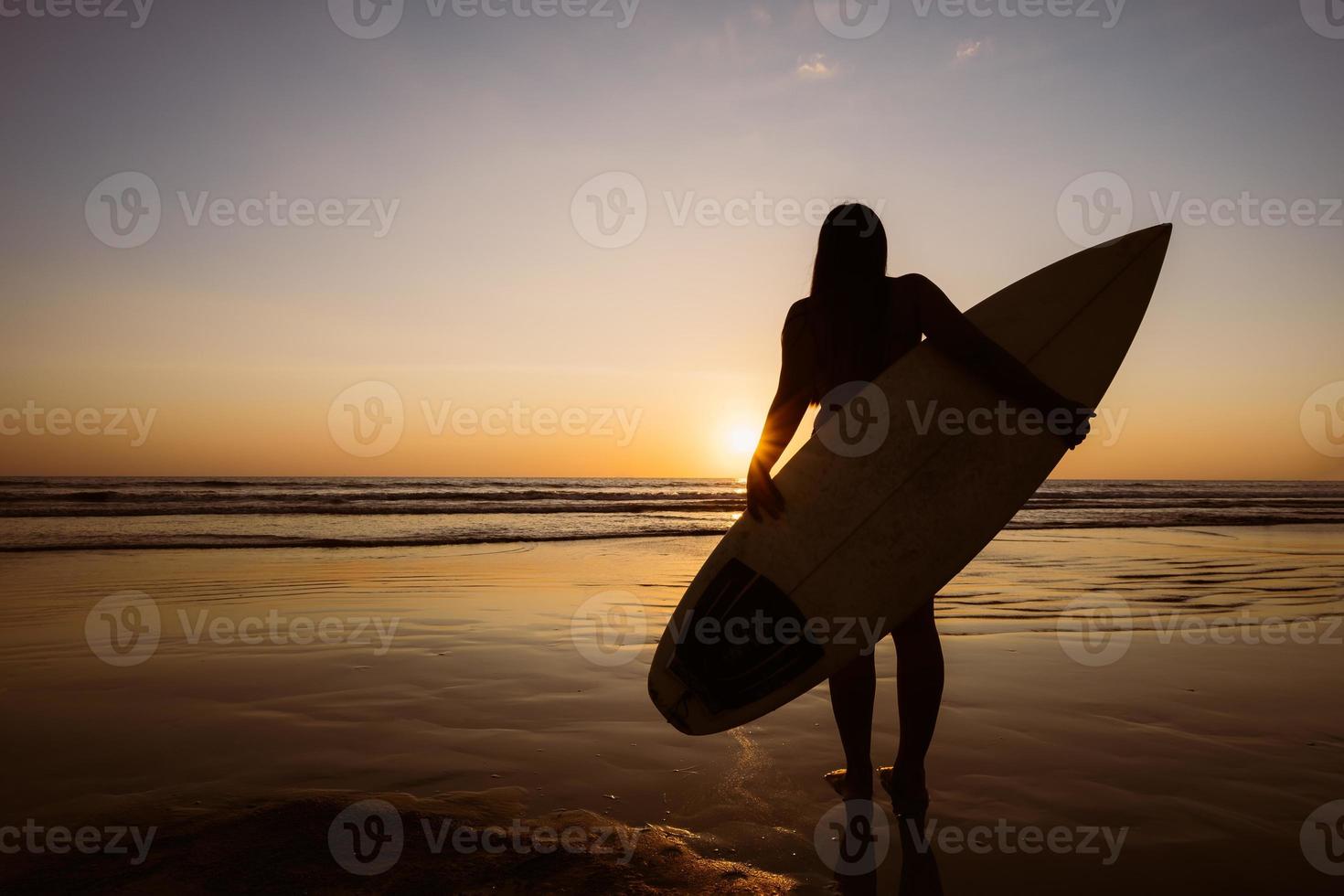 silueta de hermosa surfista sexy con tabla de surf en la playa de arena al atardecer. Deportes acuáticos. el surf es un estilo de vida saludable y activo. vacaciones de verano. foto