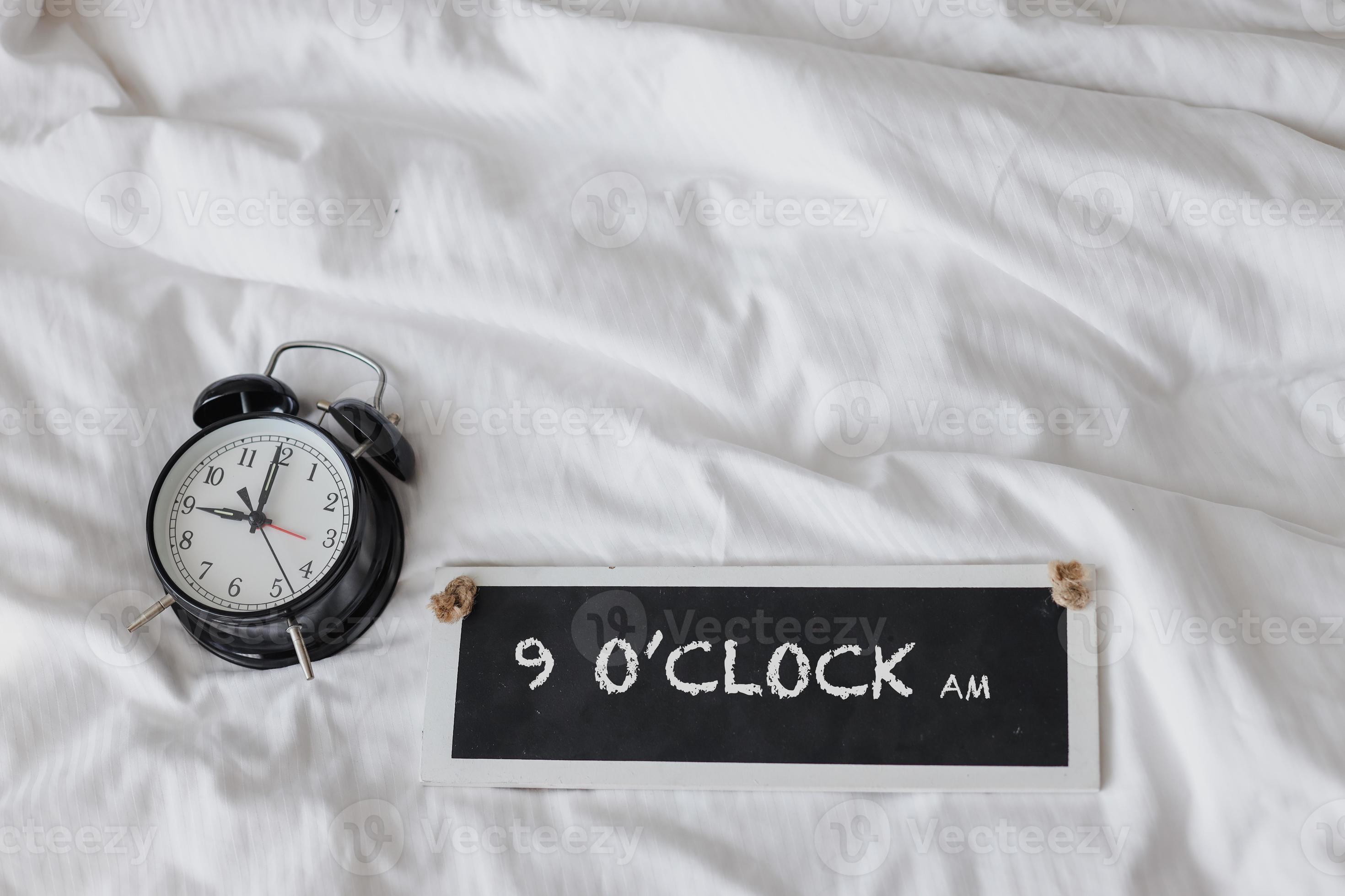 Alarm clock on the bed with sign board saying 9 oclock AM 6671050 Stock
