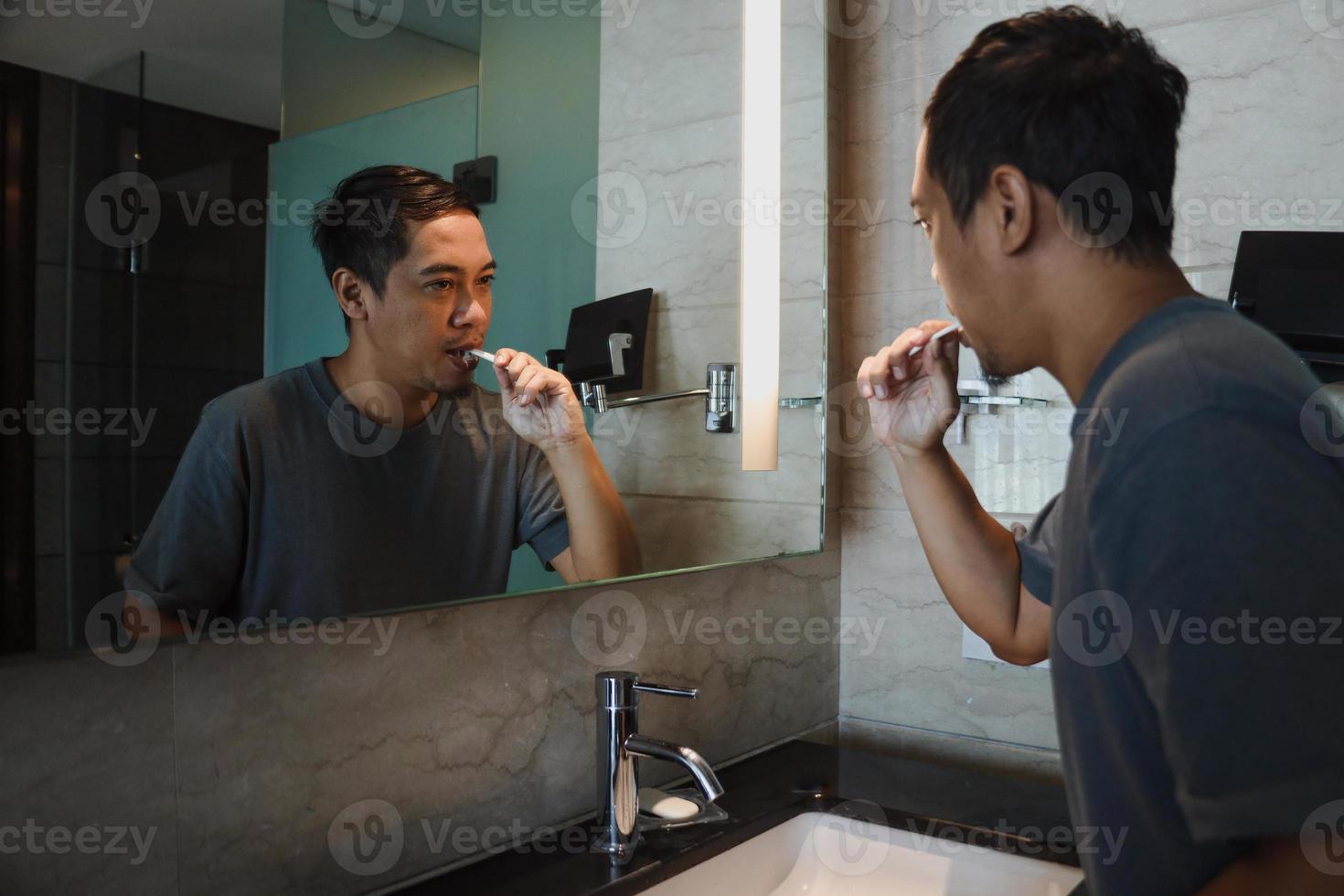 Asian man with brushing teeth and looking mirror in the bathroom photo