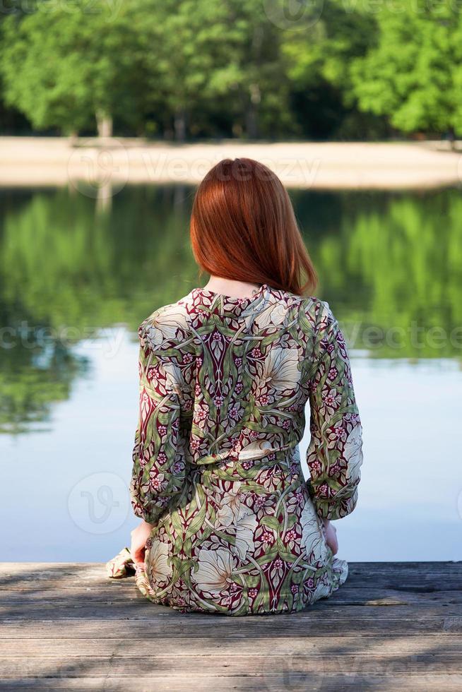mujer joven sentada en un muelle de madera mirando el lago foto