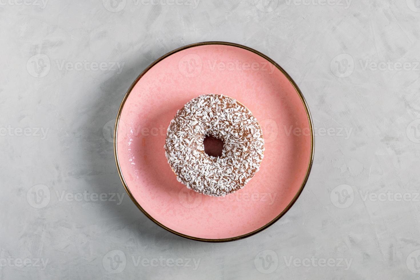 Donut with coconut topping lies on a pink ceramic plate photo