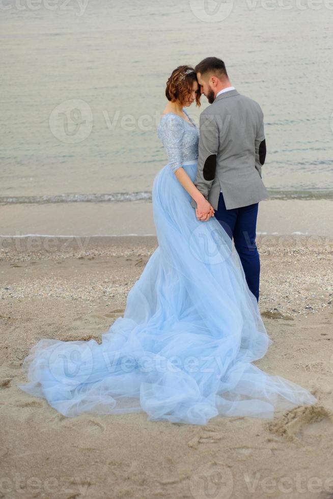 Wedding photo session of a couple on the seashore. Blue wedding dress on the bride.