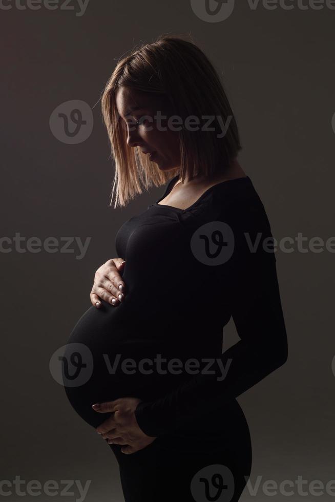 elegante hermosa mujer embarazada con un vestido negro sostiene sus manos sobre su estómago. foto