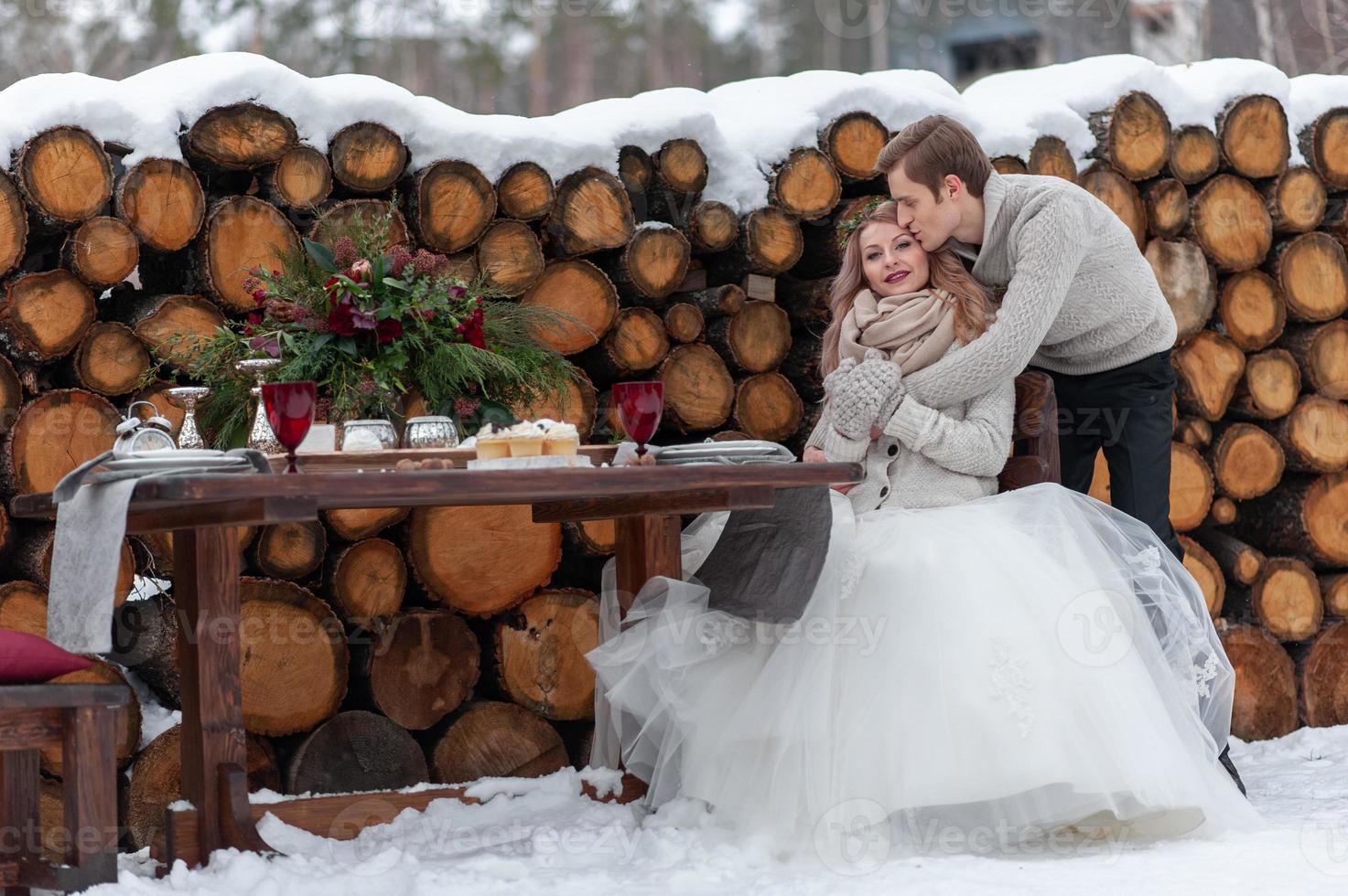 Groom is tenderly hugs his bride from the back on background of winter wedding decoration photo