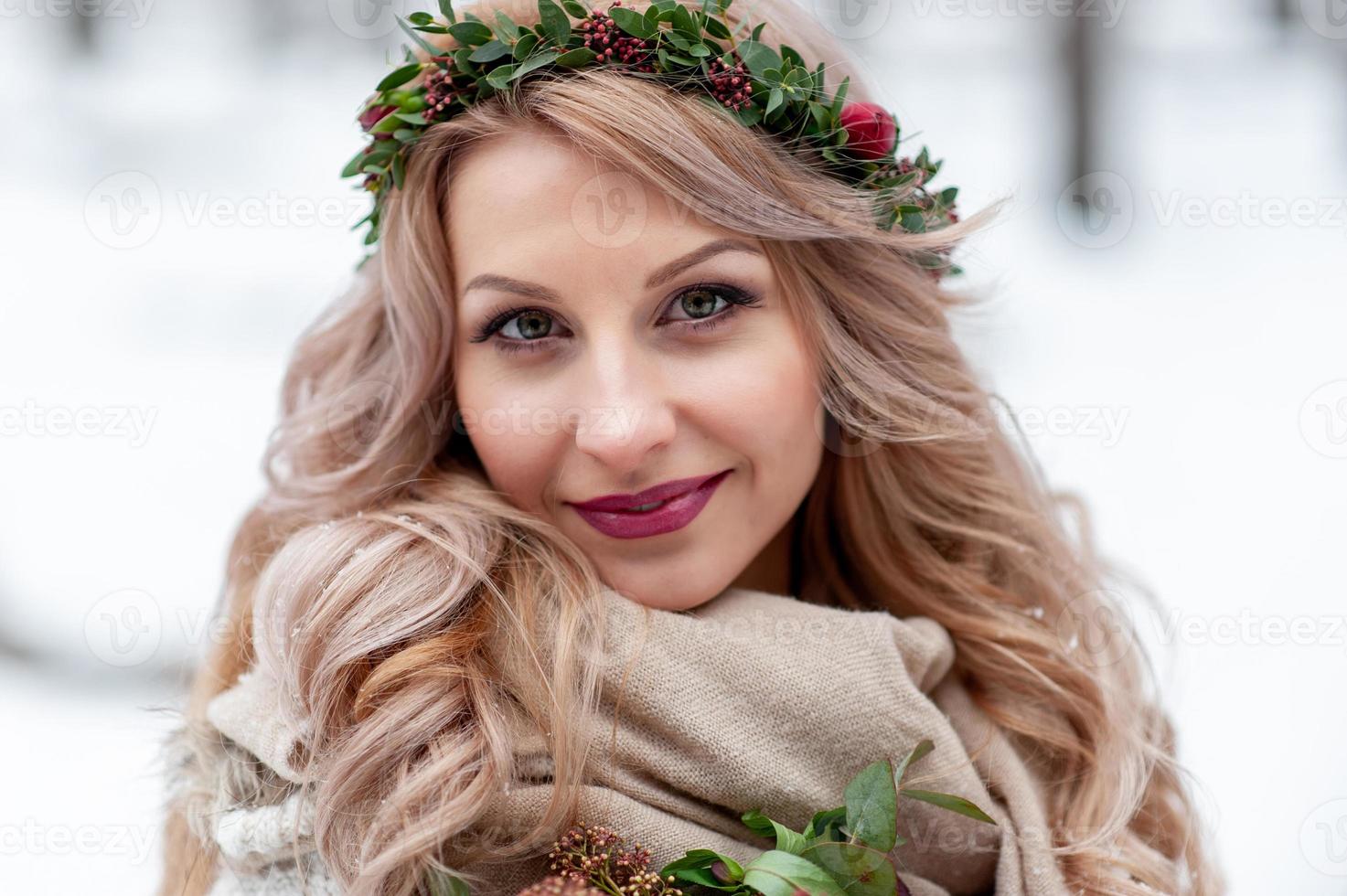 Face of a smiling girl of Slavic appearance with a wreath of wildflowers. Beautiful bride holds a bouquet in winter background. Close-up photo