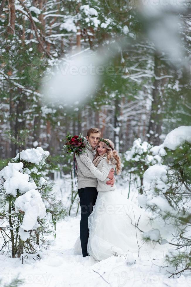 Bride and groom in beige knitted pullovers in snowy forest. Newlyweds is touching foreheads. Winter wedding. Copy space photo