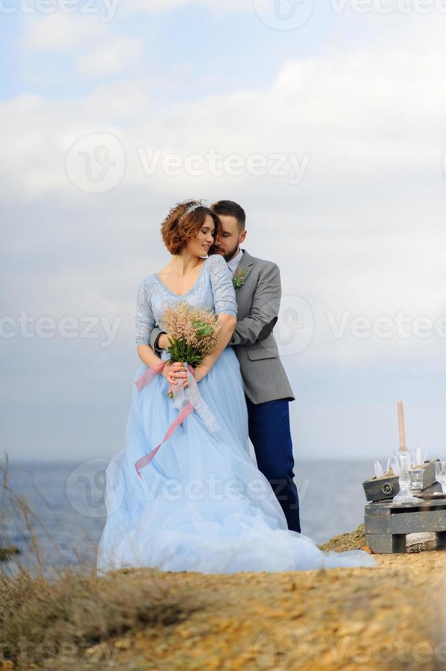 Wedding photo session of a couple on the seashore. Blue wedding dress on the bride.