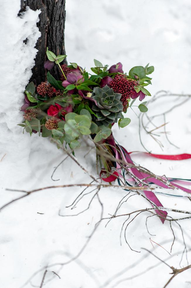 Rustic wedding bouquet with succulents and crimson flowers on the snow next to the tree. Outdoors. Artwork. Selective focus photo