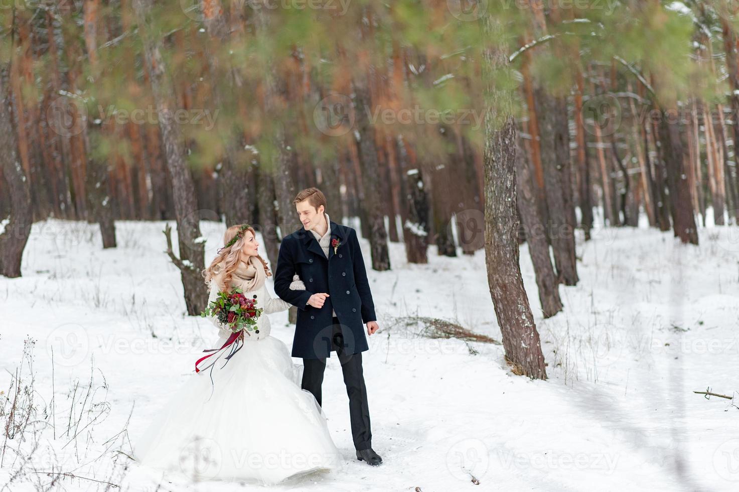 la novia y el novio alegres con jerseys de punto beige caminan en un bosque nevado. boda de invierno foto