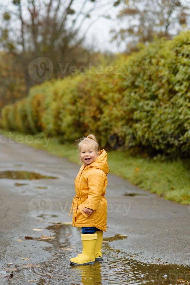 A little girl walks with an umbrella in yellow rubber boots and a waterproof raincoat. Autumn Walk. photo