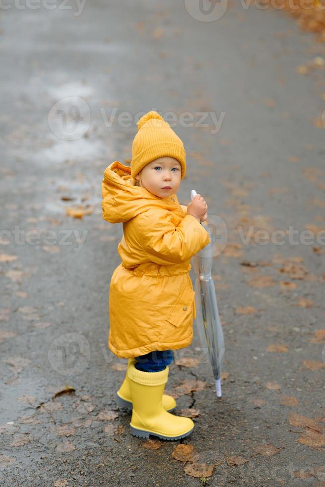 A little girl walks with an umbrella in yellow rubber boots and a waterproof raincoat. Autumn Walk. photo