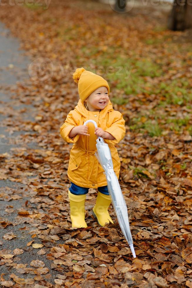 A little girl walks with an umbrella in yellow rubber boots and a waterproof raincoat. Autumn Walk. photo