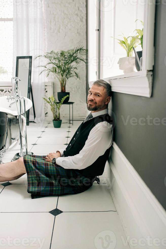 handsome mature courageous  stylish scotsman businessman in kilt and suit in bathroom. Style, work from home, fashion, lifestyle, culture, ethnic concept. photo