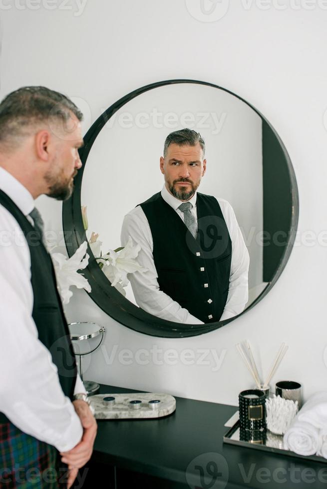 handsome mature courageous stylish man scotsman in suit by the mirror. Style, fashion, lifestyle, culture, ethnic concept. photo